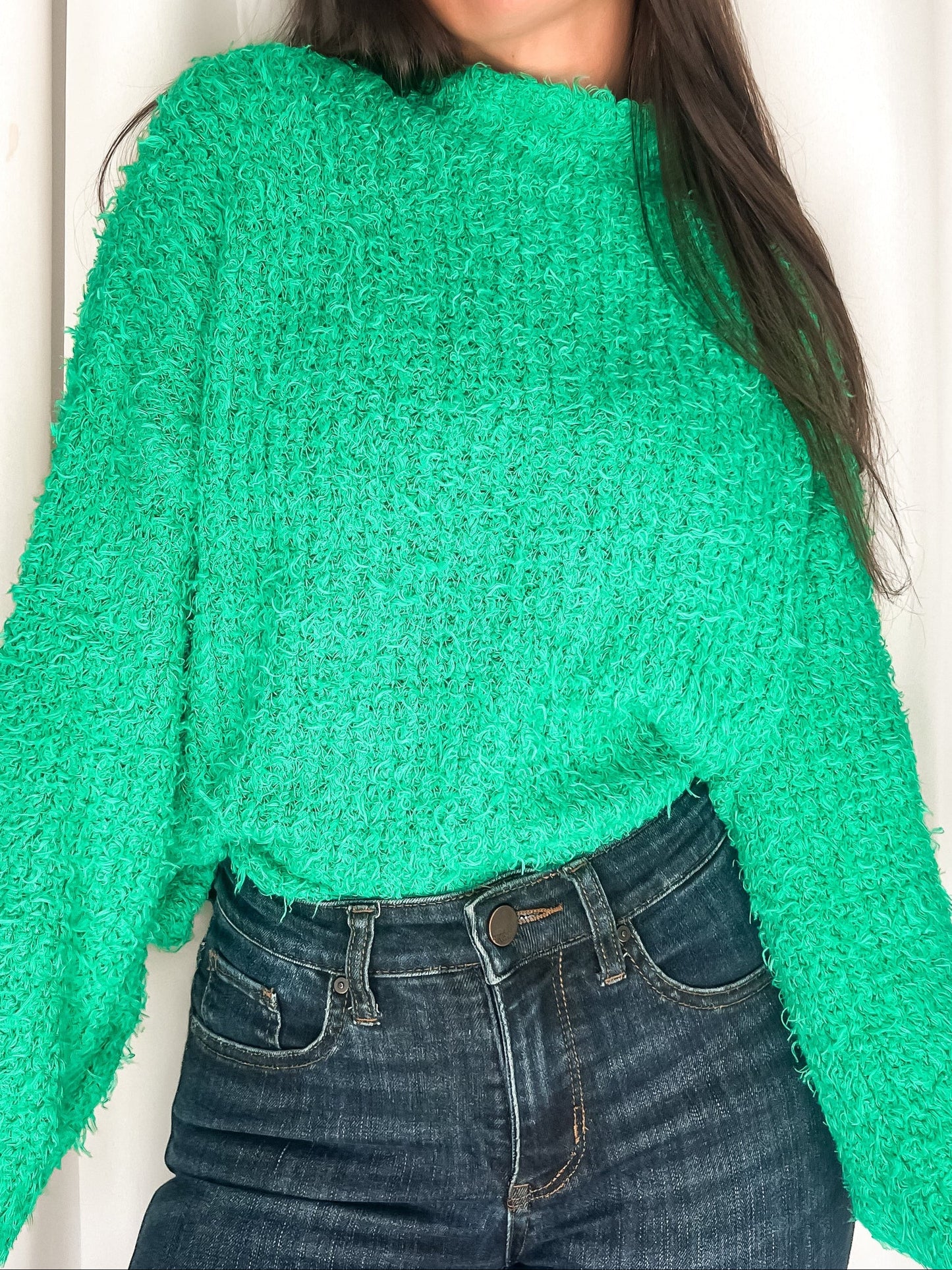 Person wearing a green textured sweater and blue jeans against a white background