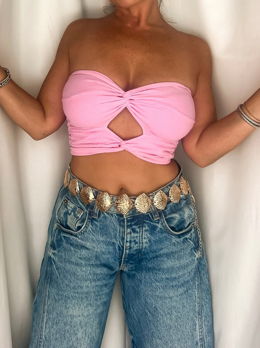 Woman wearing a pink tube top and blue jeans against a white curtain