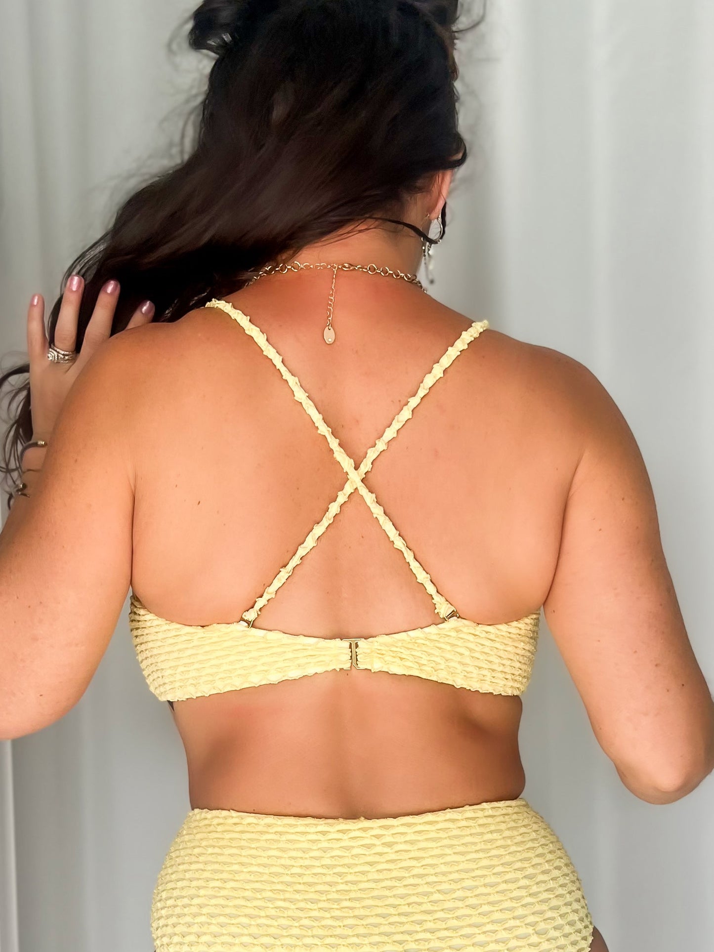 Woman wearing a yellow bikini top with criss-cross straps on the back.