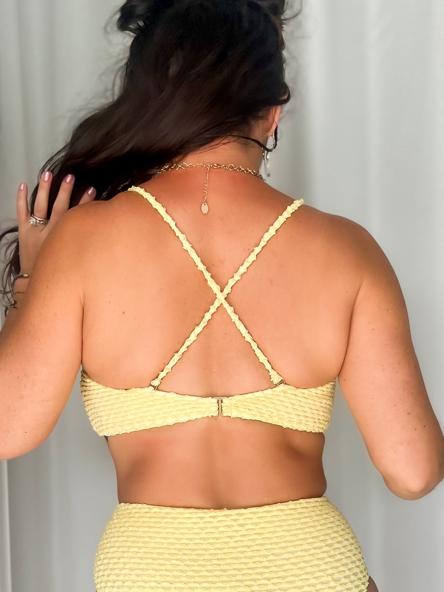 Woman wearing a yellow bikini top with criss-cross straps on the back.